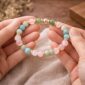 Hands holding a Love and Connection gemstone bracelet with rose quartz, amazonite, and green aventurine beads
