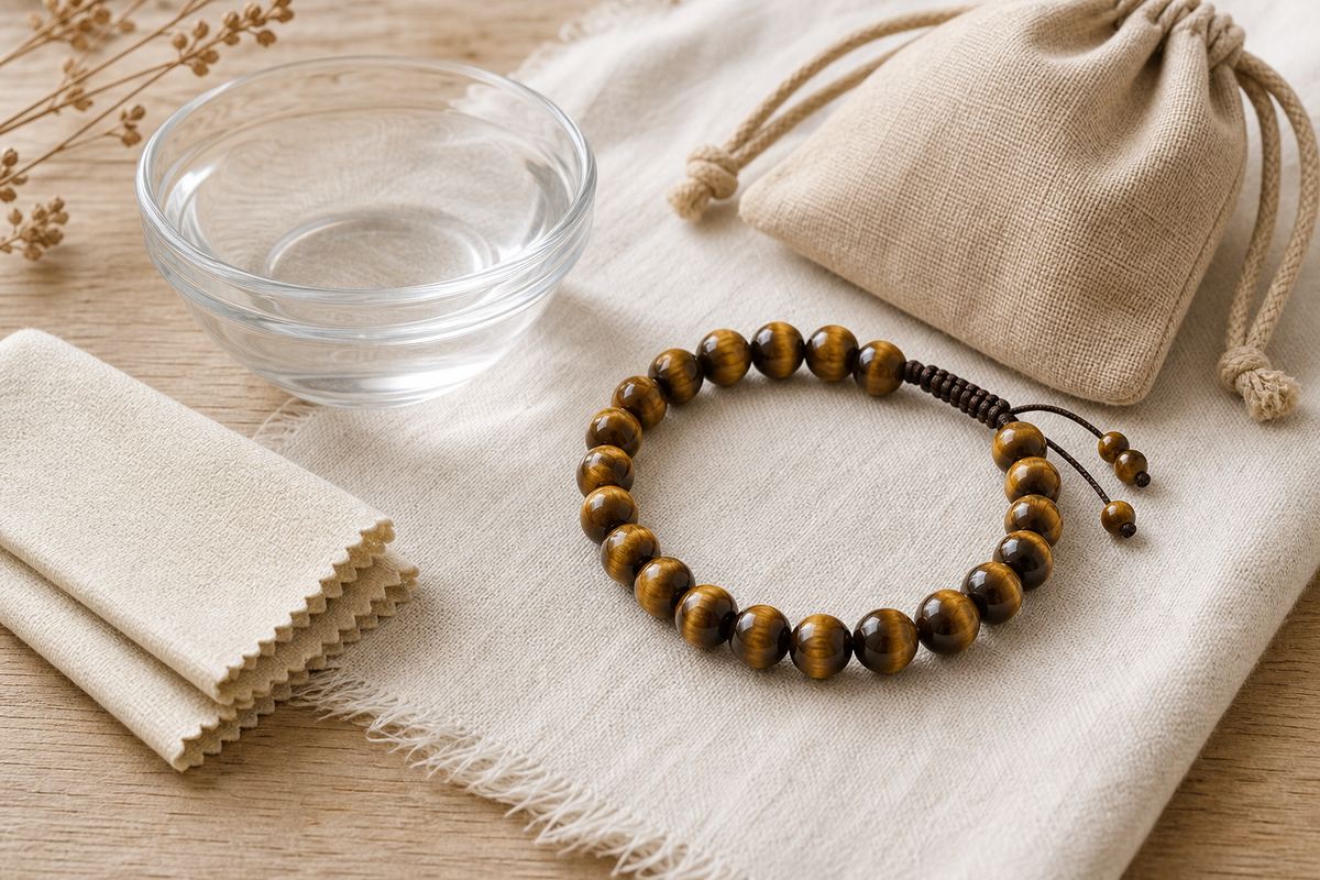 Tiger eye bracelet beside a soft cloth, clear water bowl, and neutral storage pouch