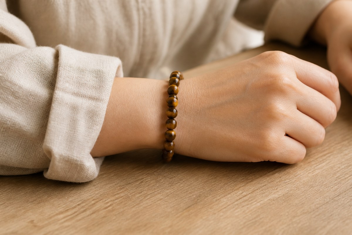 Anonymous wrist wearing a golden-brown tiger eye bead bracelet with neutral linen clothing