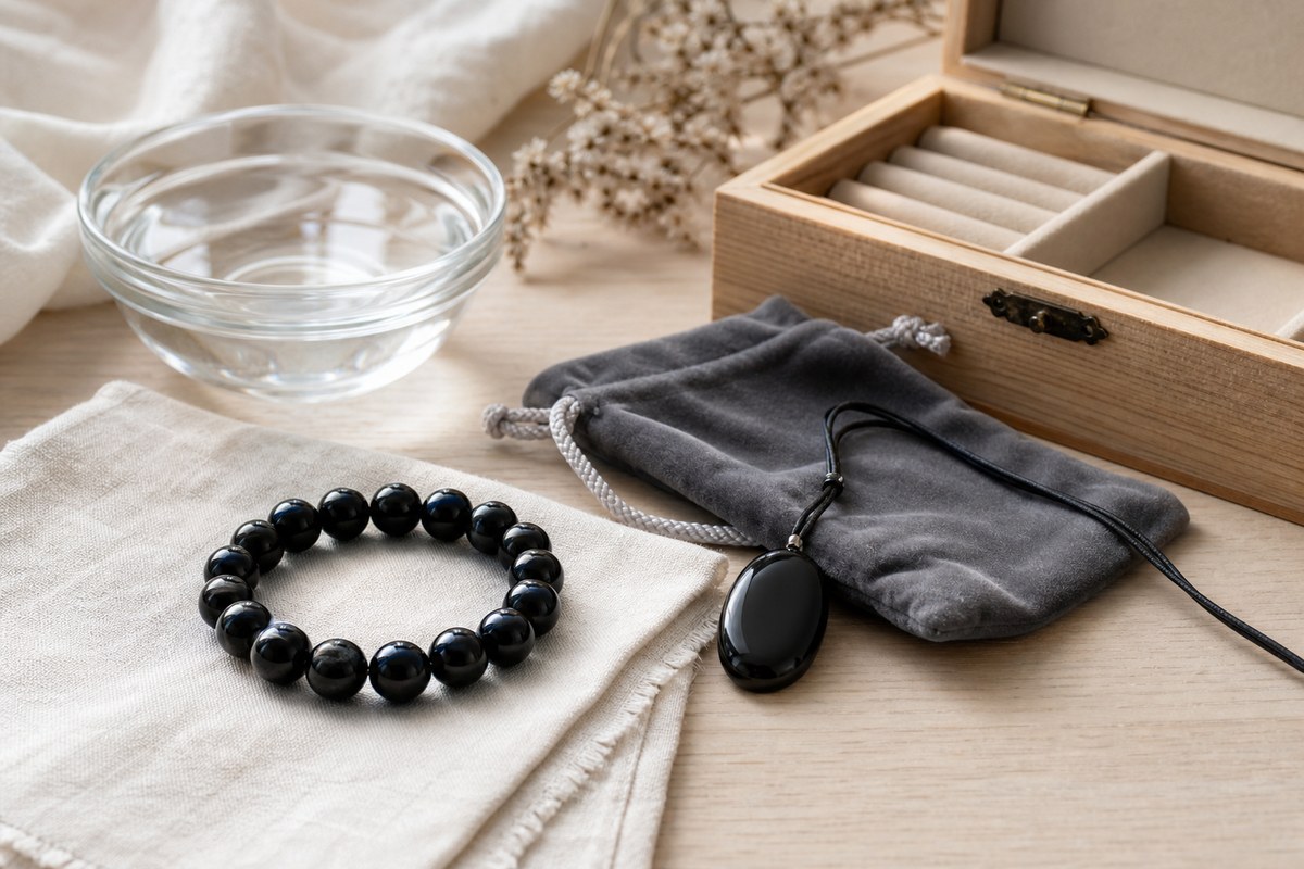 Black obsidian bracelet beside a soft cloth, water bowl, pouch, and wooden jewelry box