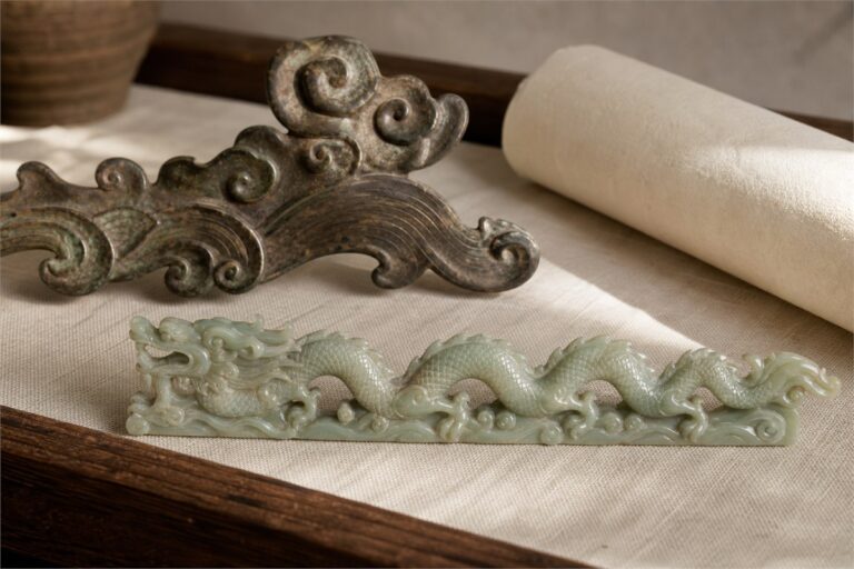 Museum-inspired Chinese dragon motif carved in jade beside aged bronze and handmade paper on warm linen