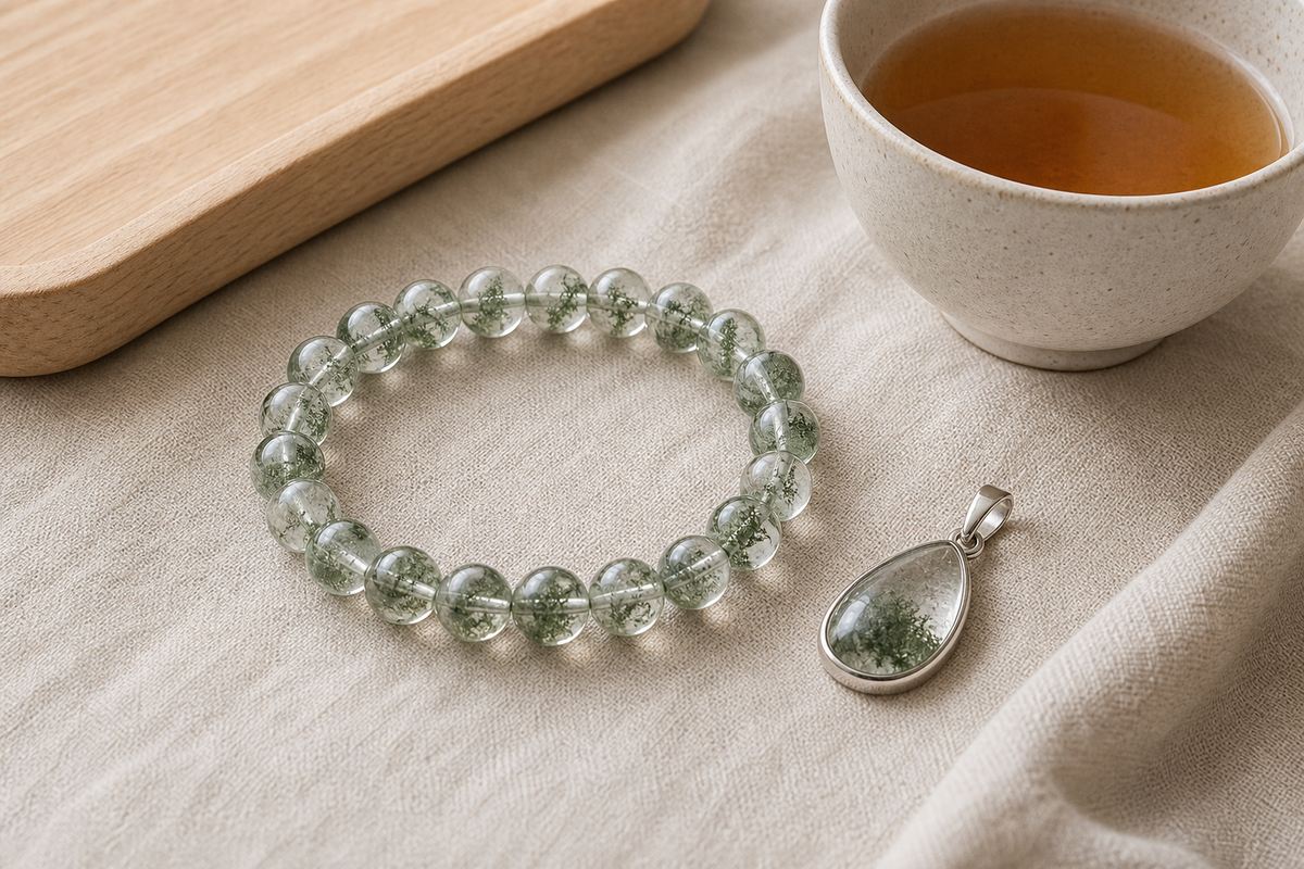 Green phantom quartz bracelet and pendant on ivory linen beside a ceramic tea cup