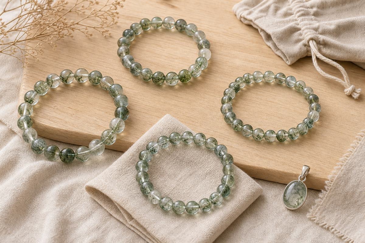 Green phantom quartz bracelet on a wooden desk beside a closed notebook and ceramic cup