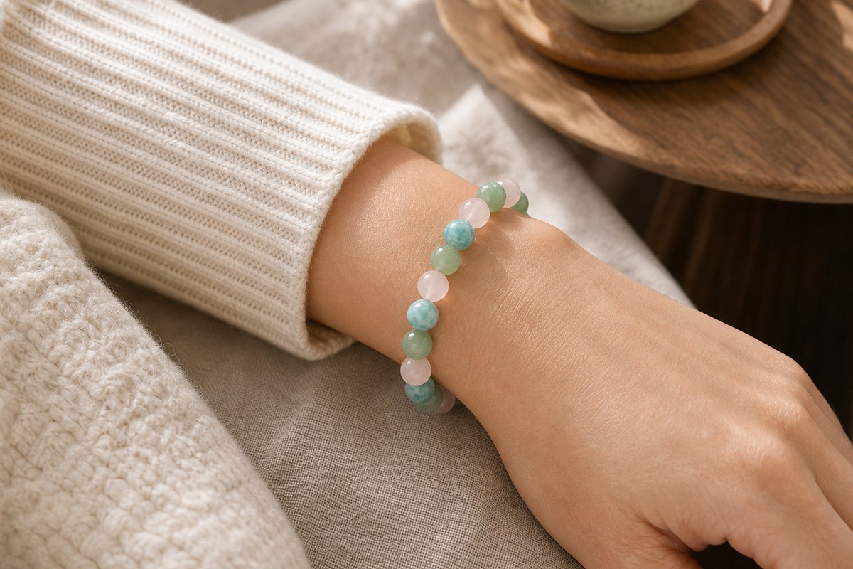 Anonymous wrist wearing a rose quartz, amazonite, and green aventurine bracelet with a cream knit sleeve