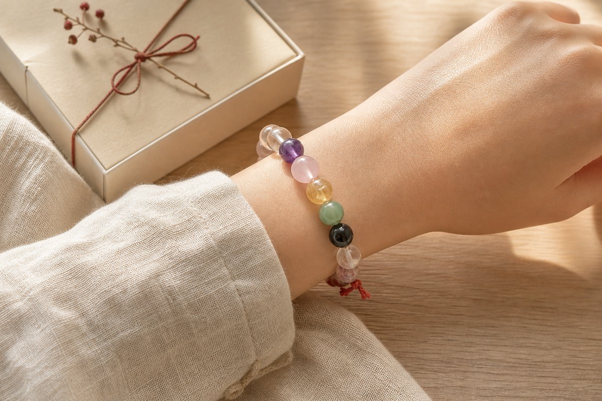 Anonymous wrist wearing a mixed crystal bracelet beside a neutral gift box on pale wood