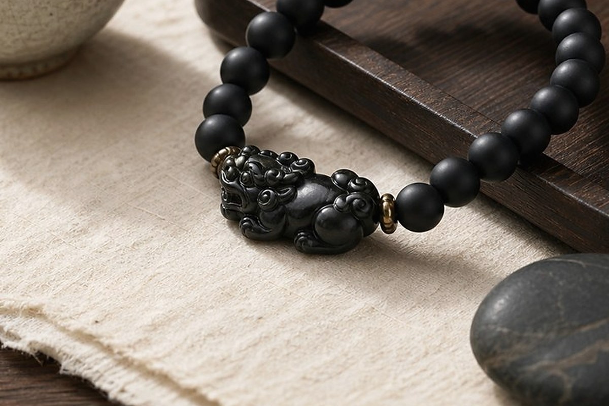 Close view of a carved black Pixiu charm on an obsidian bead bracelet