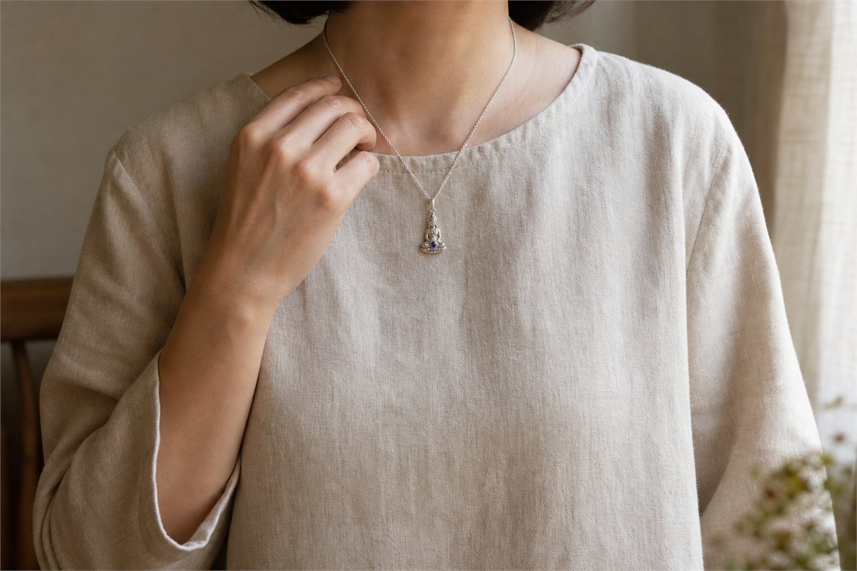 Adult wearing a small silver bodhisattva pendant over plain linen clothing