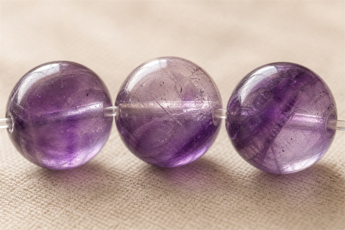 Macro view of three amethyst beads showing internal purple color bands and inclusions