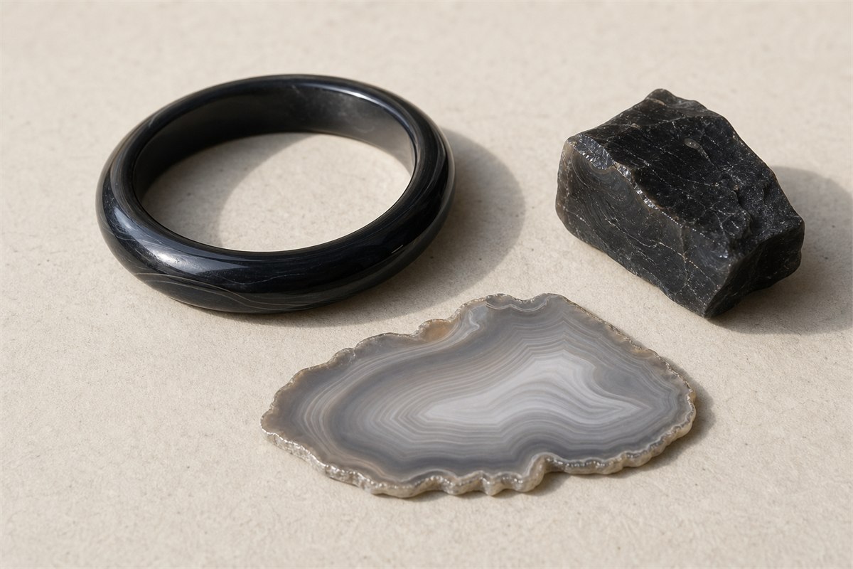 Black agate bangle beside dark chalcedony rough and a pale banded agate slice