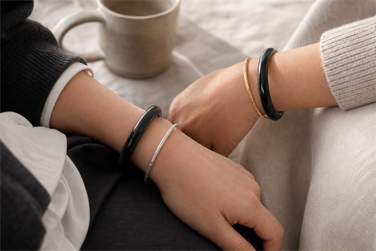 Black agate bangle styled separately with a slim silver bracelet and a soft gold bracelet