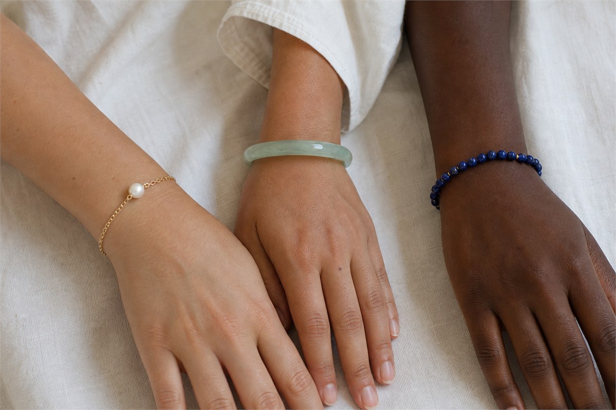 Three wrists with different skin tones wearing pearl gold, pale green jade, and blue bead bracelets