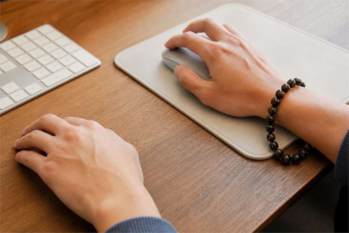 Right hand using a mouse while a loose dark bead bracelet touches the mouse pad