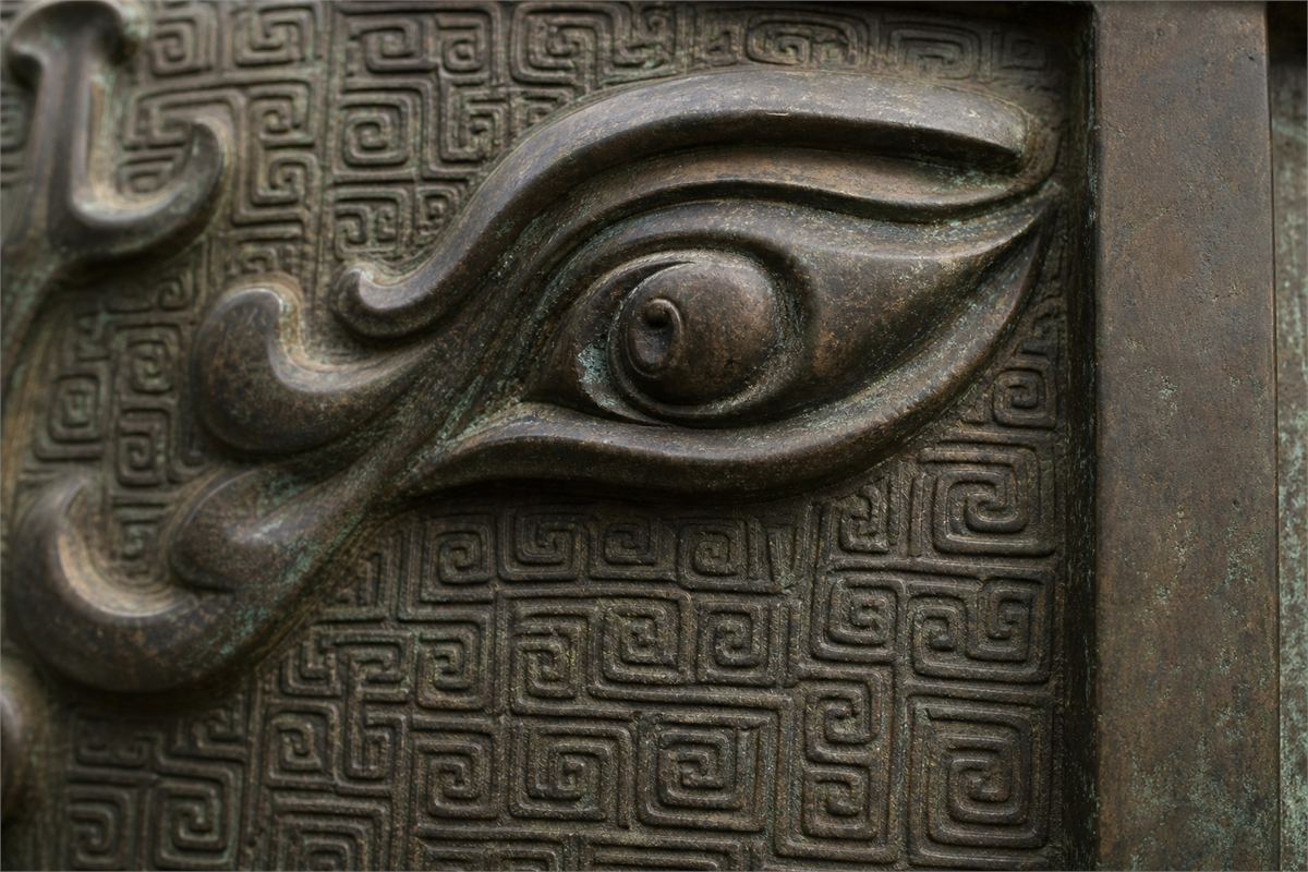 Raised bronze animal eye and brow above a dense recessed field of small squared spirals