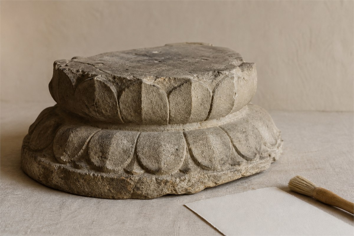 Unoccupied carved stone double-lotus pedestal fragment on neutral conservation linen