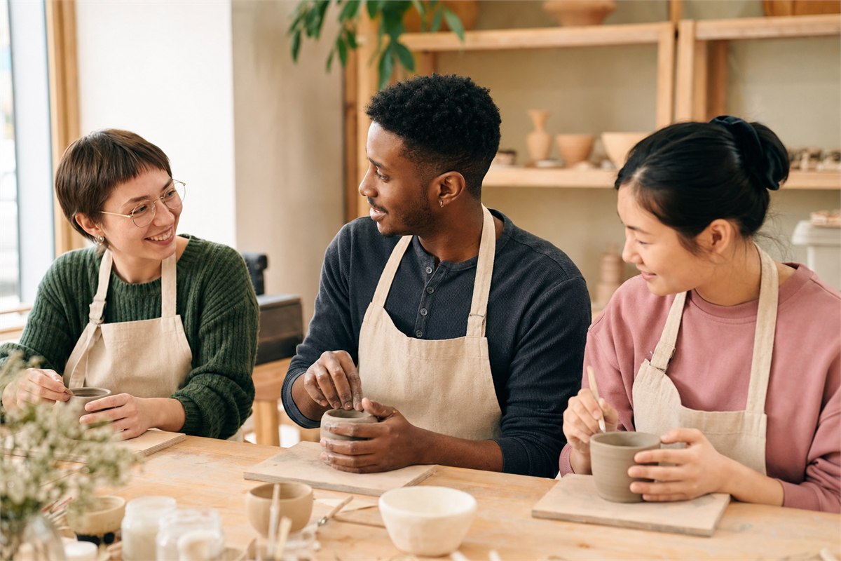 Three adults talking naturally during a bright community pottery class