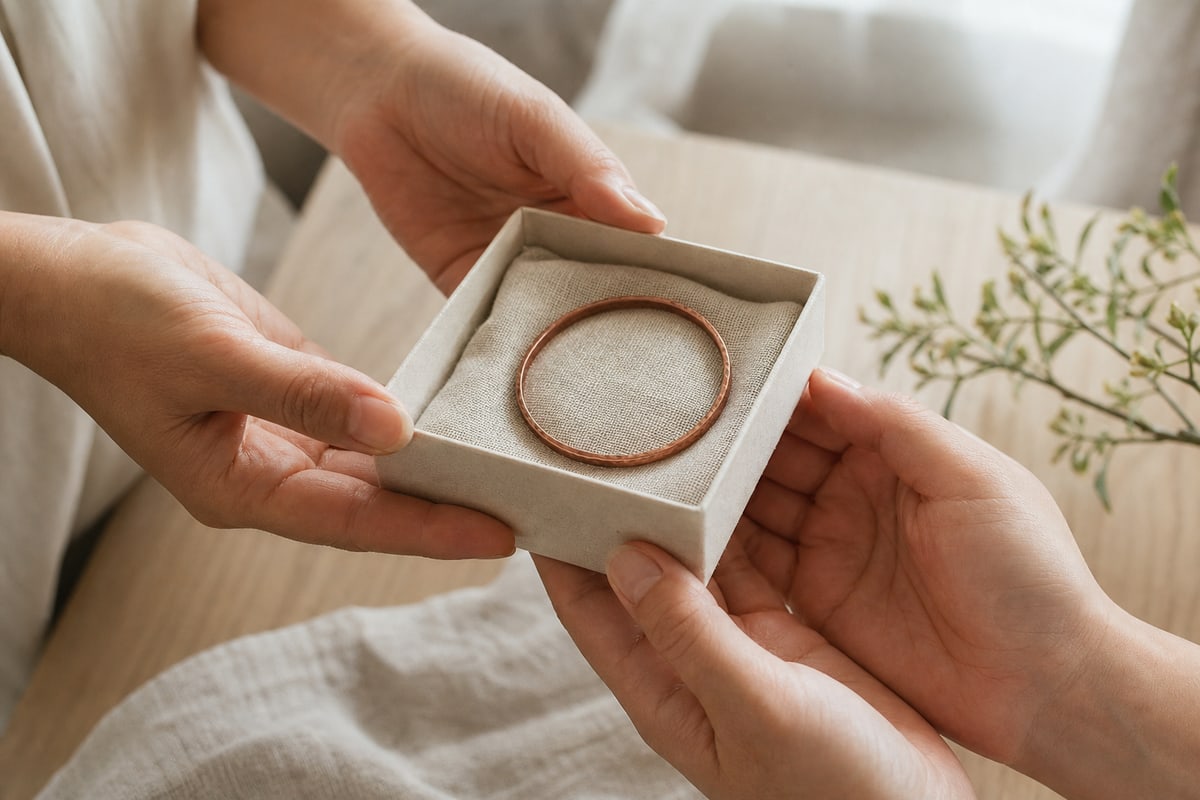Four hands exchanging a linen lined gift box with one hammered copper bracelet