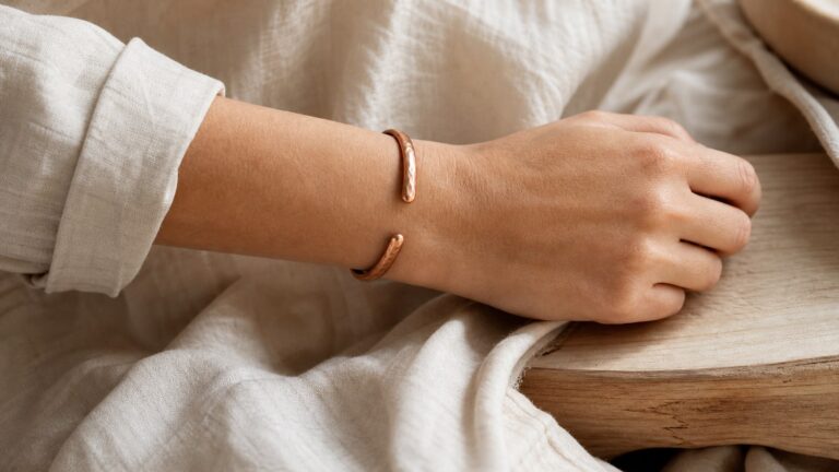 Hammered red copper cuff worn on an adult wrist beside cream linen and pale wood
