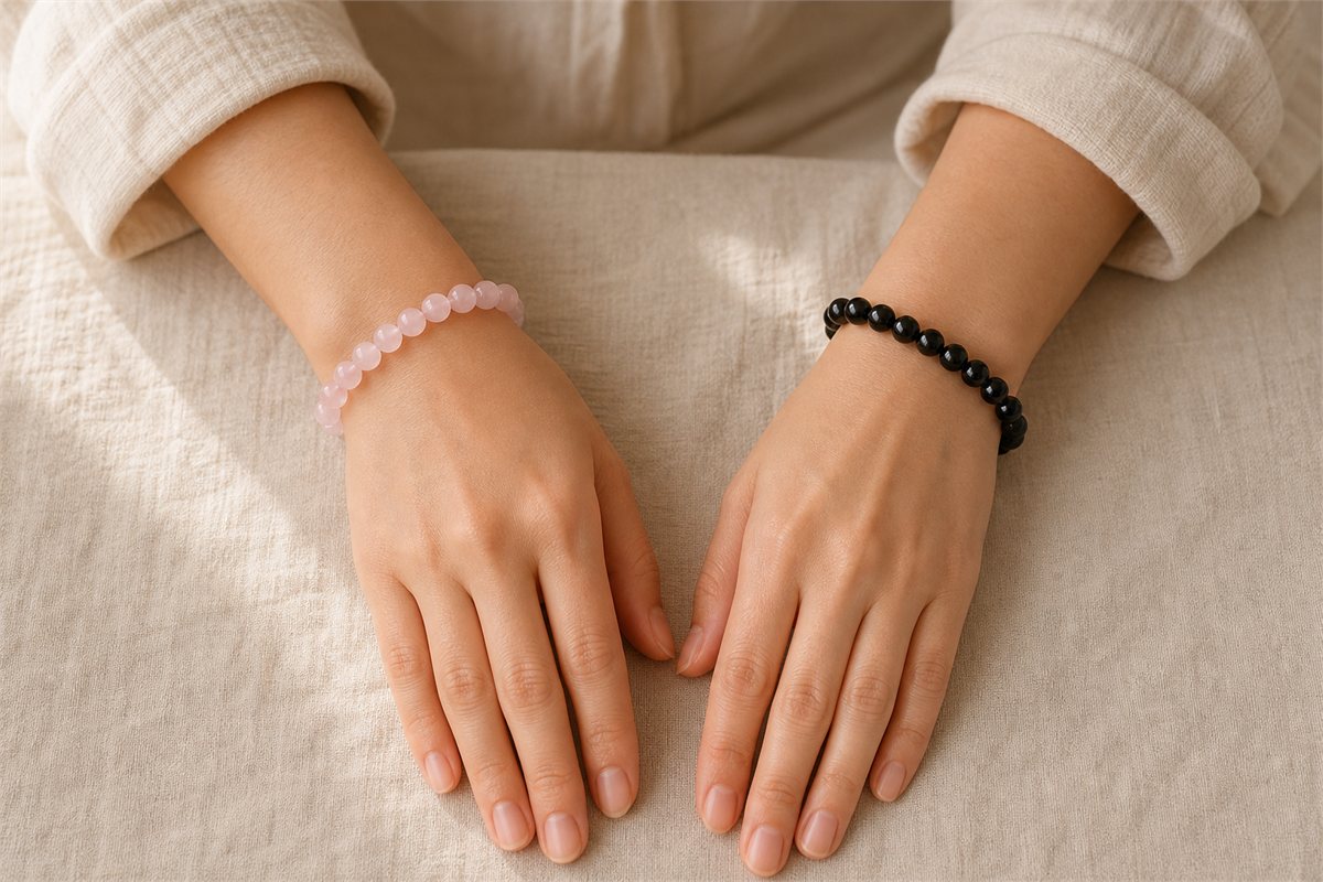 The same person wearing a rose quartz bracelet on one wrist and a black obsidian bracelet on the other