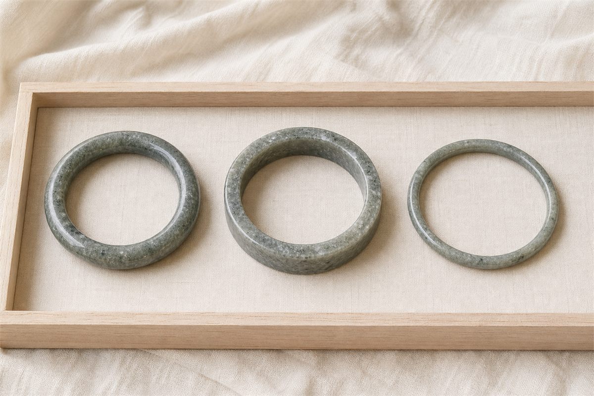 Three gray-green quartzite bangles with round, wide, and slim profiles on a pale wood tray