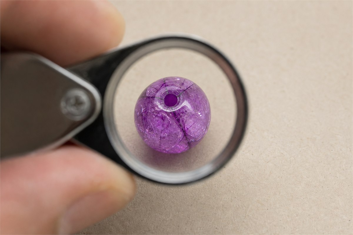 Loupe inspection of a brightly colored crackle bead with dye concentrated along sharp fractures and the drill hole