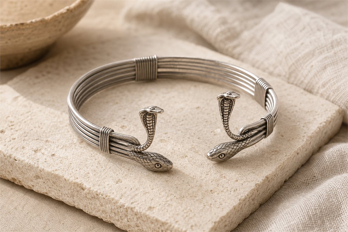 Silver bound-wire armlet with rearing cobra motifs and snake-head terminals on pale linen