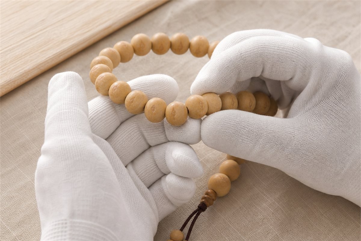 White cotton-gloved hands gently turning pale Fengyan Bodhi beads during initial surface cleaning