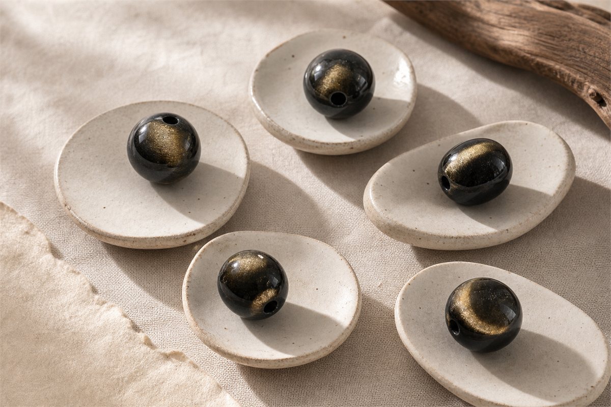 Five gold sheen obsidian beads showing sparse, broad, eye-like, opposing, and near-circular reflections