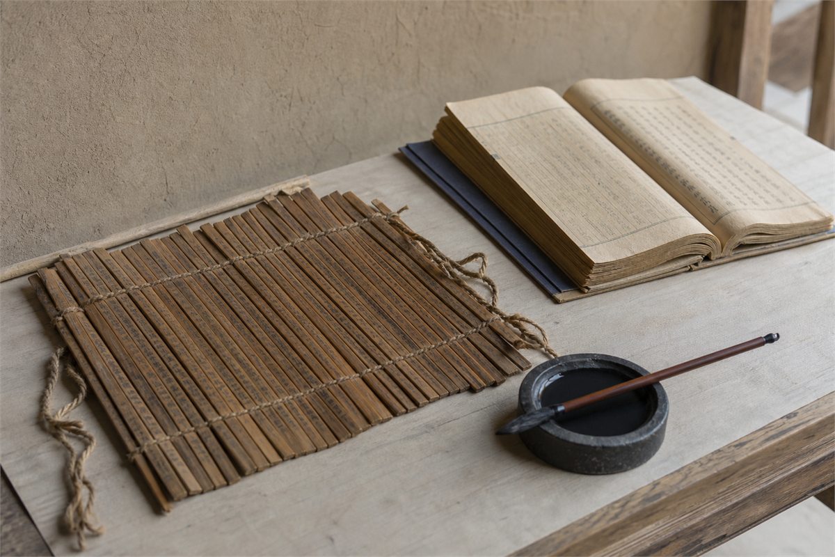 Aged bamboo slips and a later bound commentary beside an inkstone on a quiet archive table