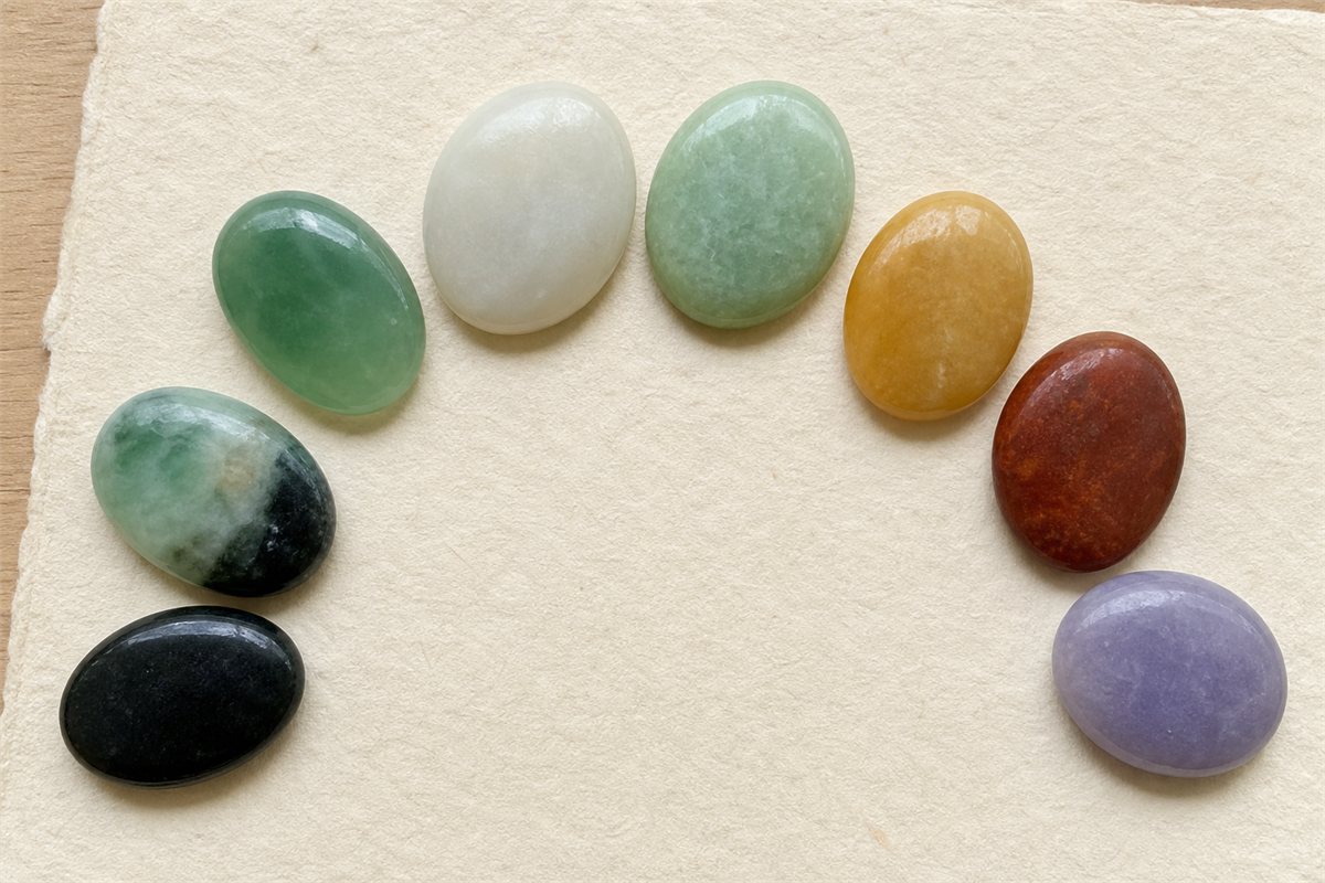 Eight polished jade samples in green, white, celadon, yellow, russet, lavender, black, and variegated colors arranged on ivory paper