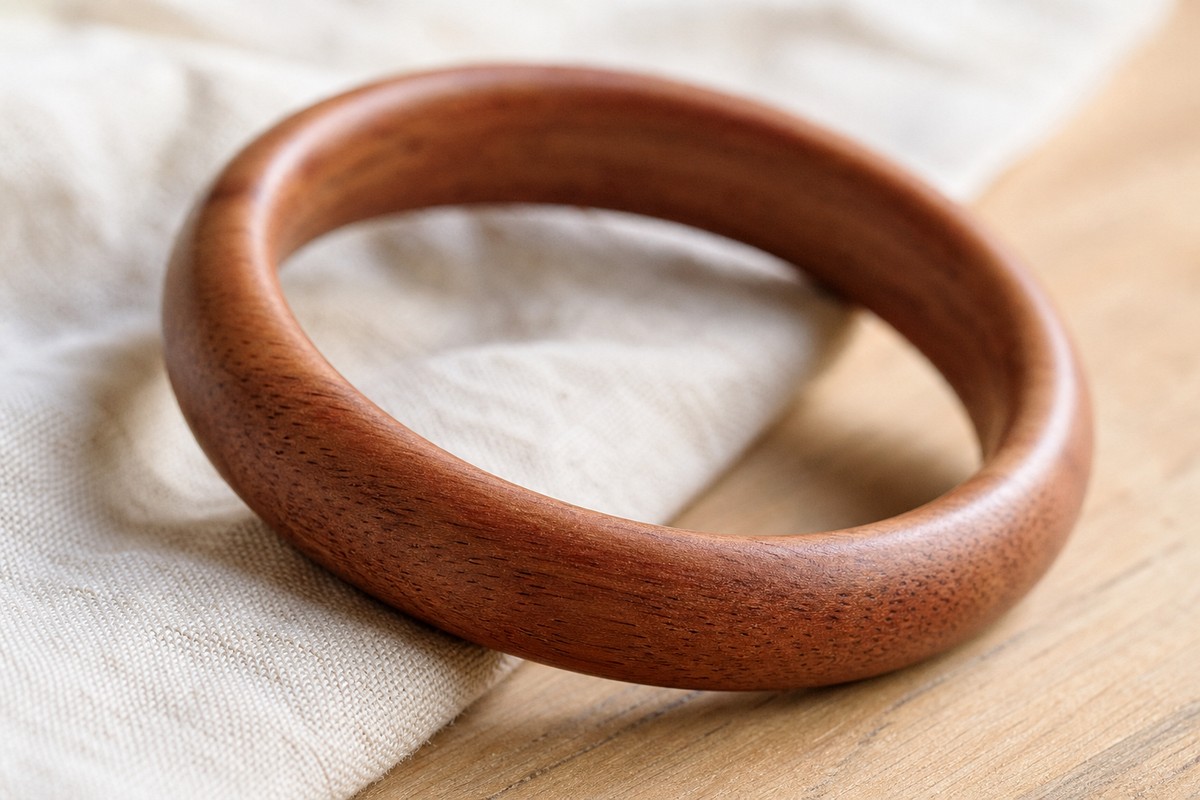 Close view of a peach wood bangle bracelet showing reddish brown grain and rounded polish