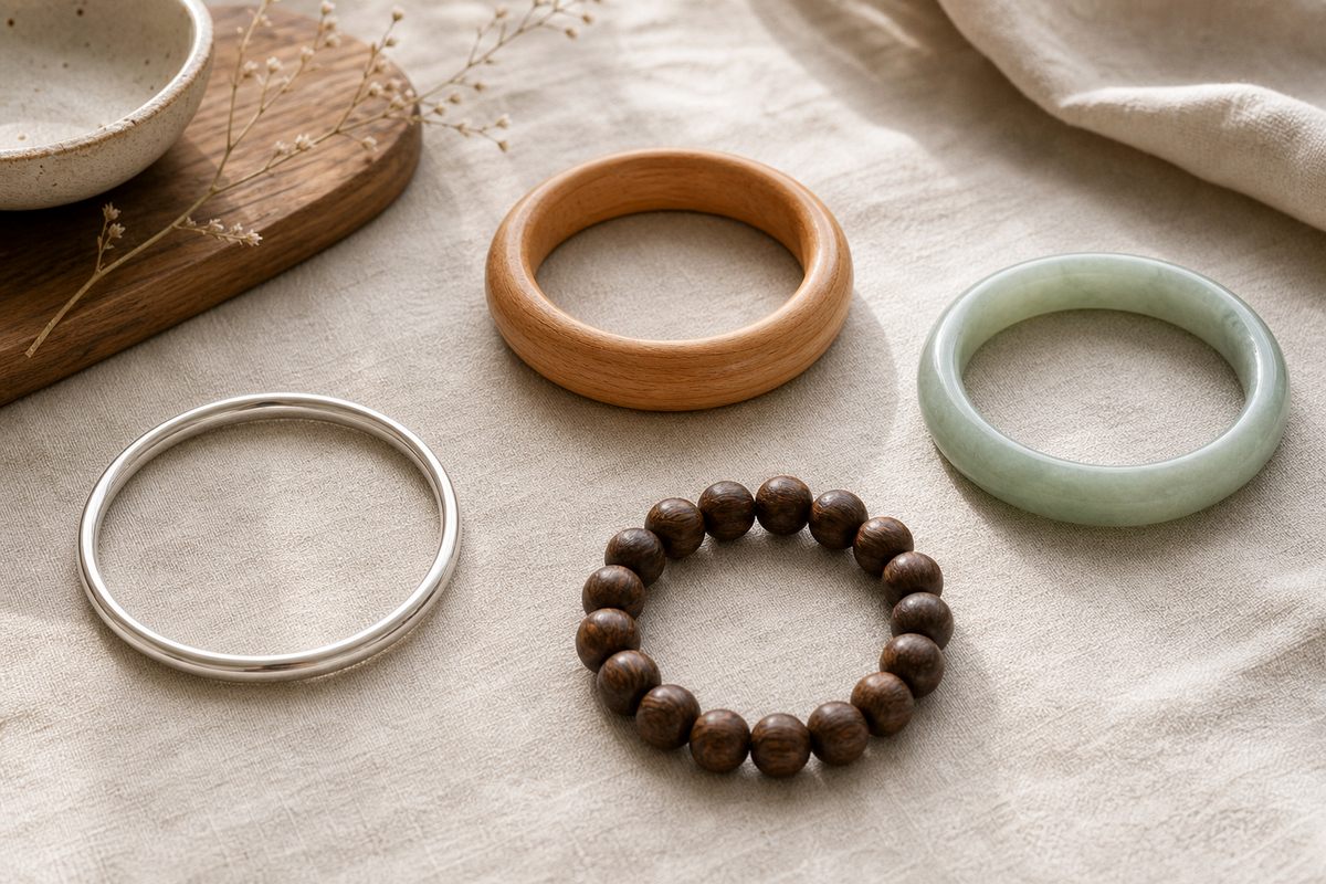 Peach wood, darker wood beads, silver, and pale green jade bracelets arranged separately on neutral linen