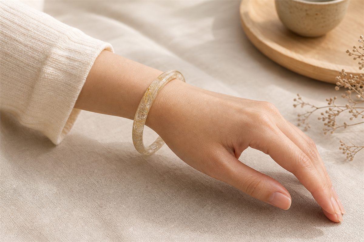 Closed rutilated quartz bangle resting loosely above a relaxed wrist without pressing into the skin