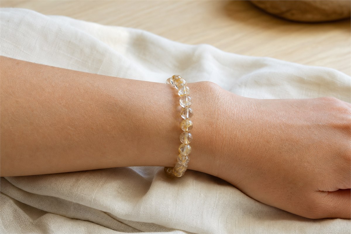Transparent rutilated quartz bead bracelet resting comfortably around an adult wrist on ivory linen