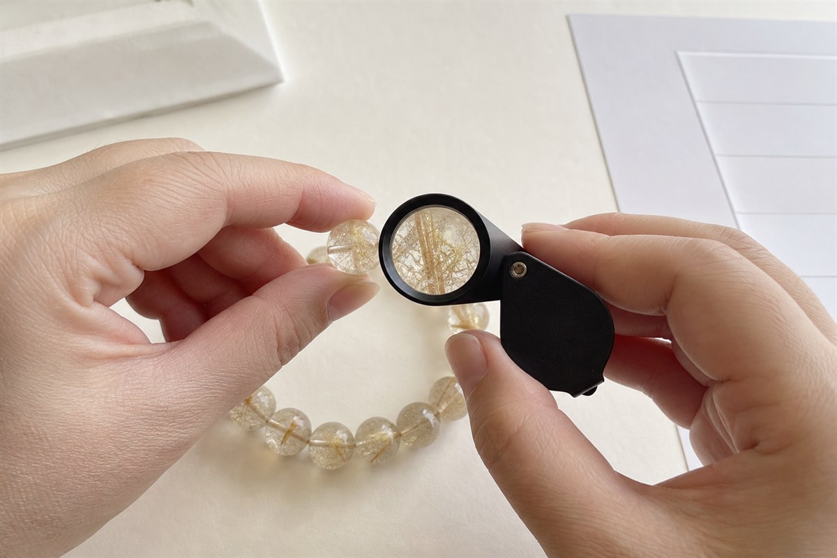 Jewelry professional examining three-dimensional rutile inclusions in a quartz bead with a 10x loupe