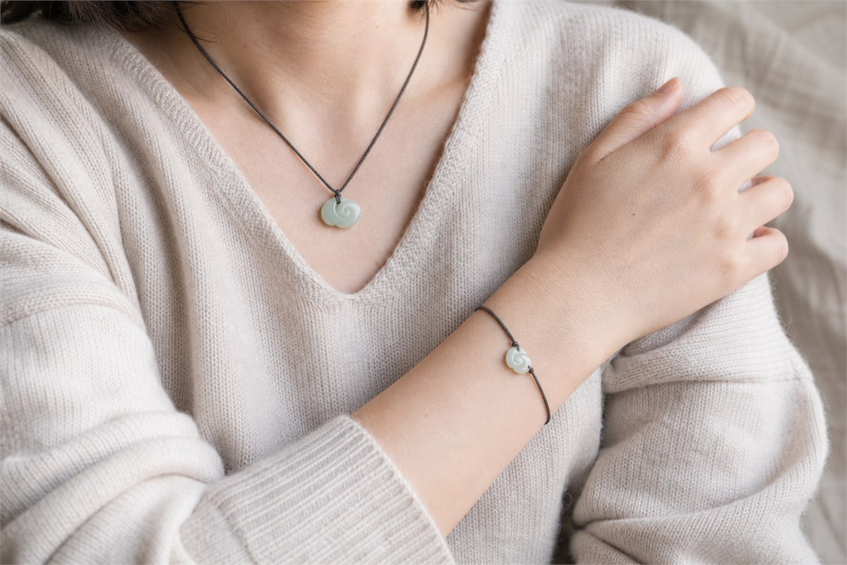 Small pale jade ruyi-cloud pendant and bracelet charm worn with a neutral knit