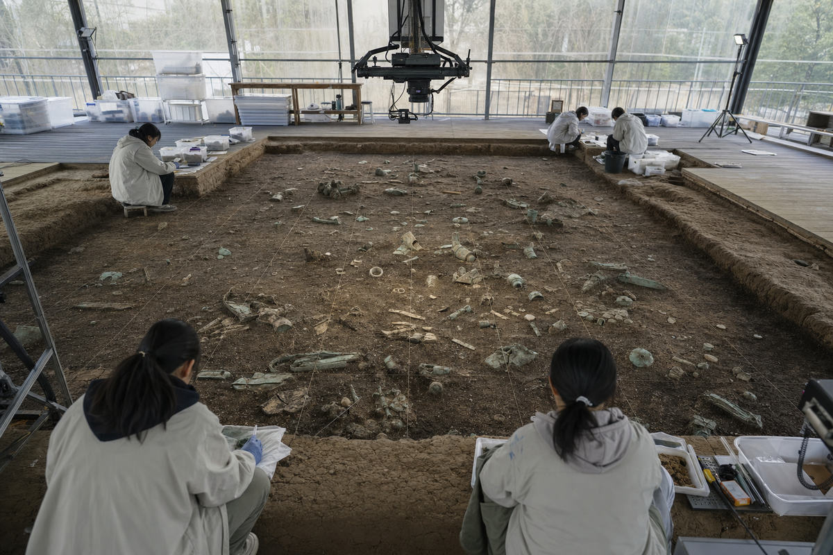 Conservators documenting separated fragments in a gridded excavation pit inside a protective cabin