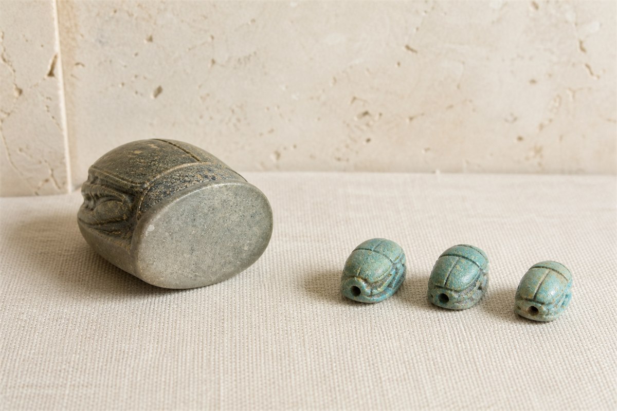 Plain-based stone scarab seal beside three small pierced blue-green scarab amulets.