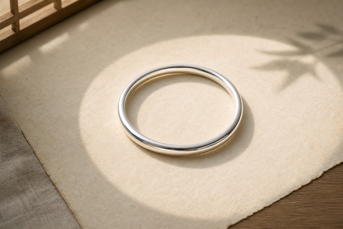 A round silver bangle centered in a soft circle of daylight on warm parchment.