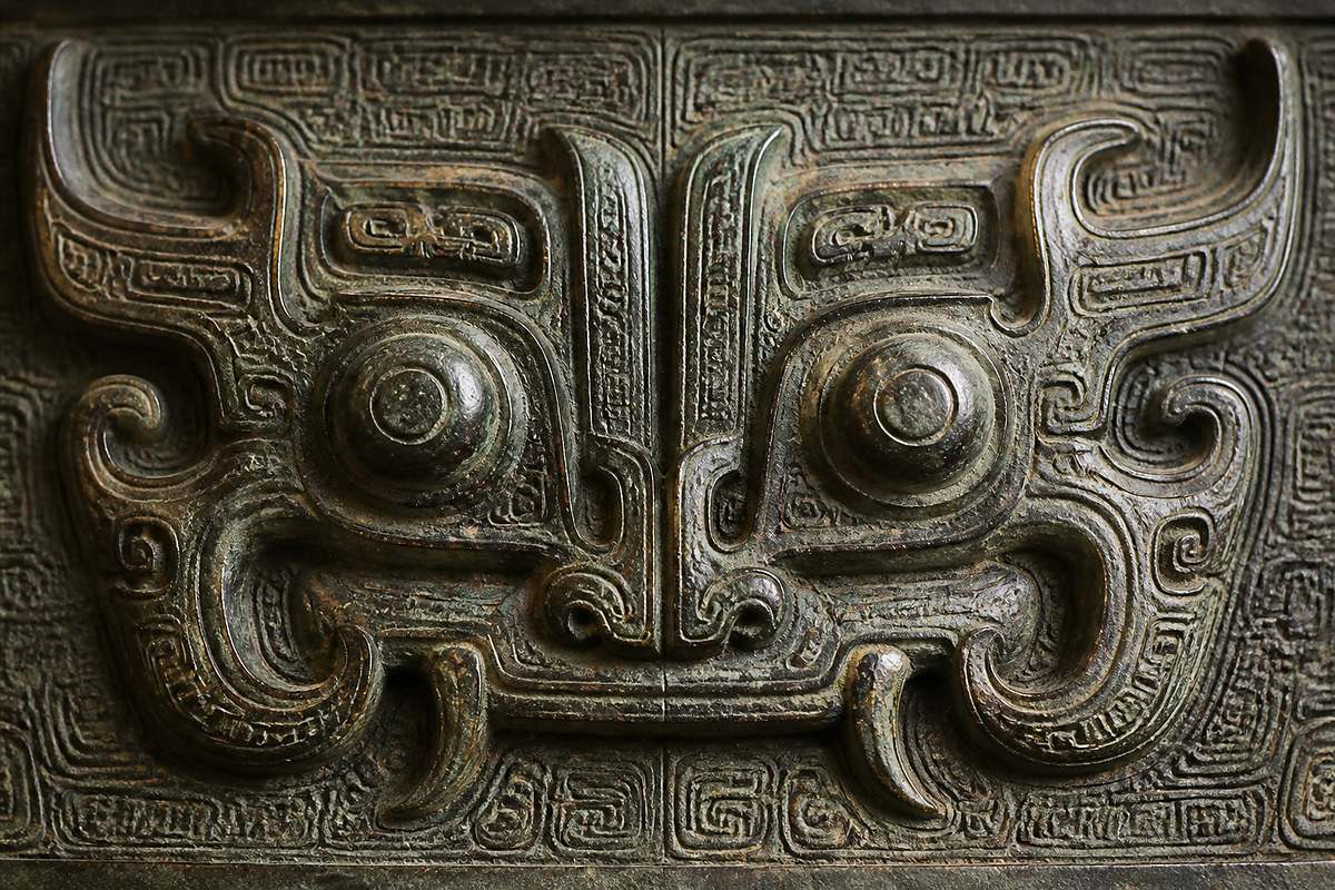 Taotie pattern (饕餮纹) close-up with huge eyes, horns, fangs, and Yun Lei Wen (云雷纹)