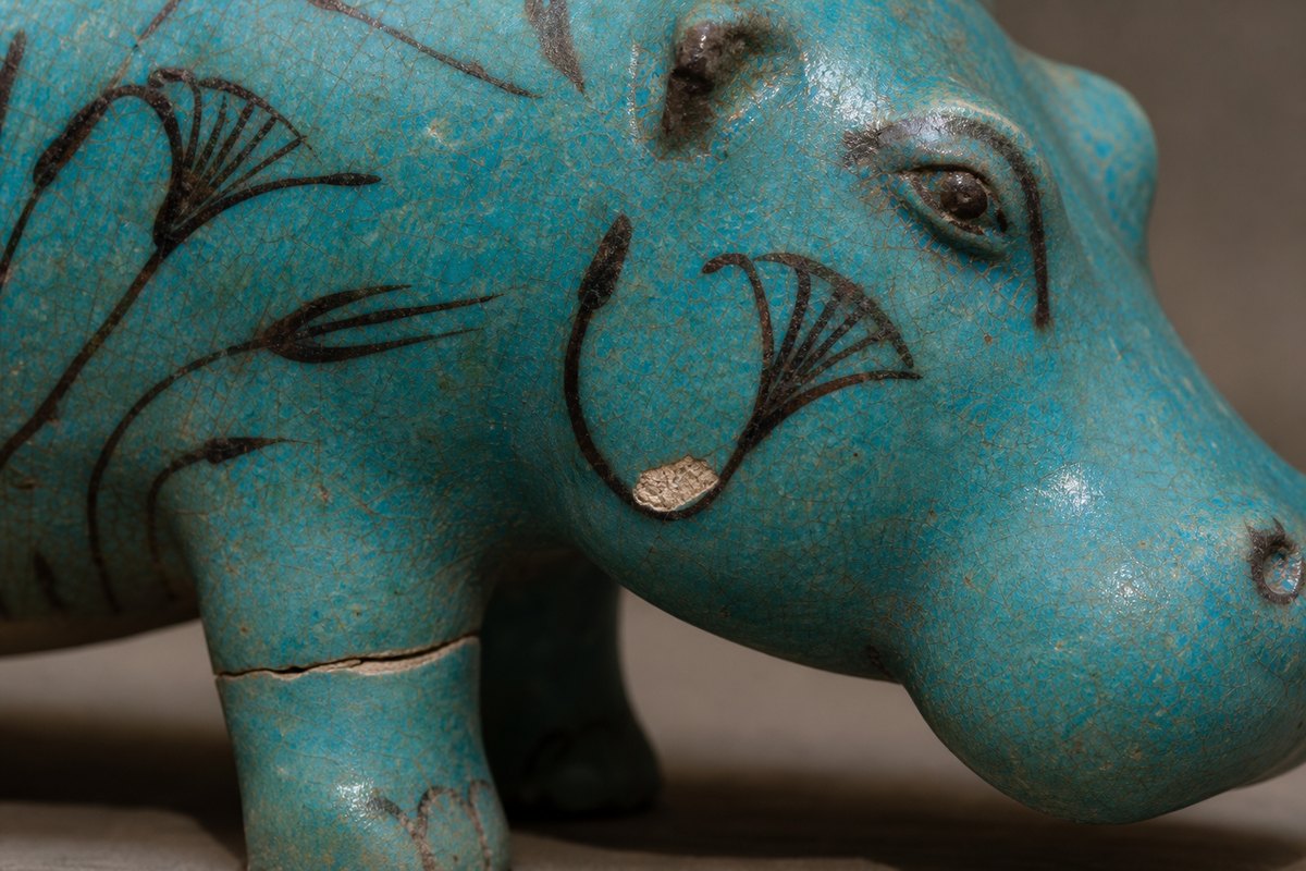 Close view of blue-green faience glaze, pale quartz-rich core, painted plant line, and restored leg join