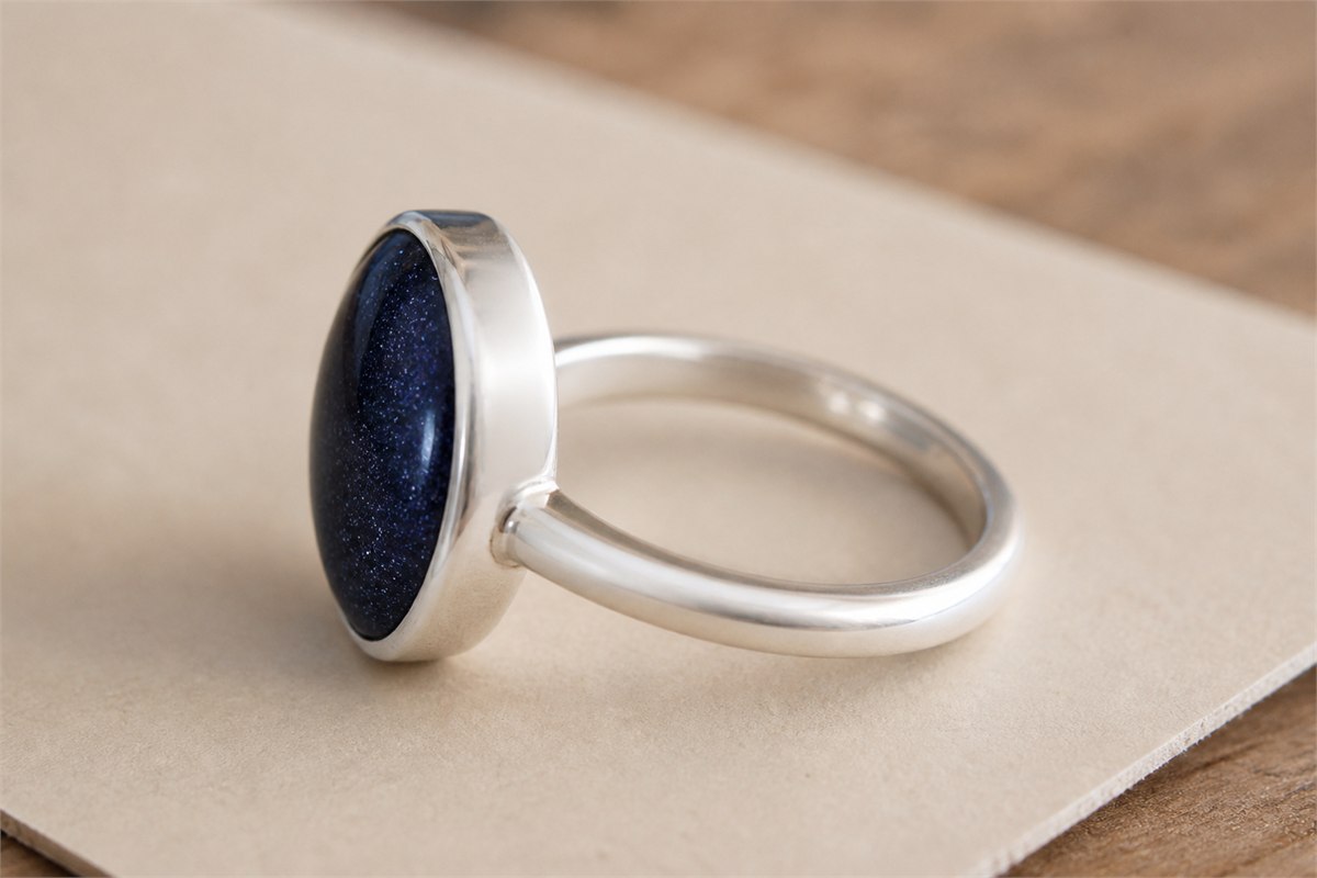 Side view of a blue goldstone cabochon secured by a low silver bezel and rounded band