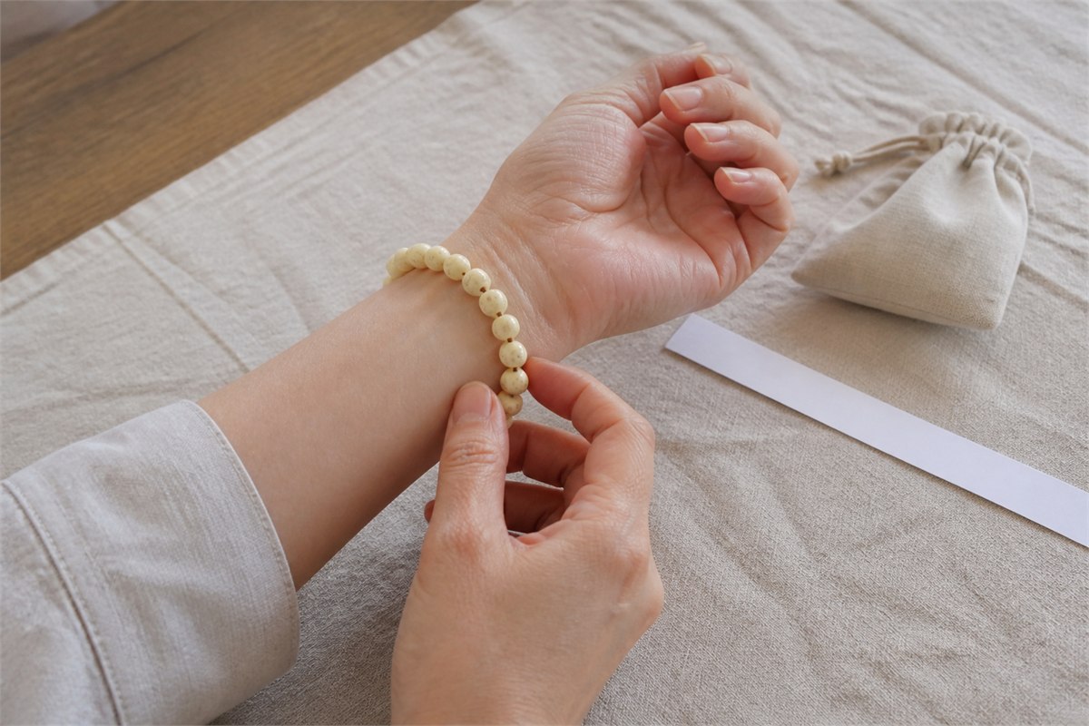 Hands checking an ivory seed-bead bracelet fit with a blank paper strip