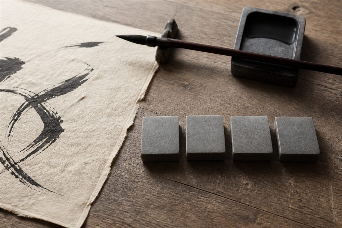Calligraphy brush, inkstone, and four stone blanks beside abstract unreadable brush marks