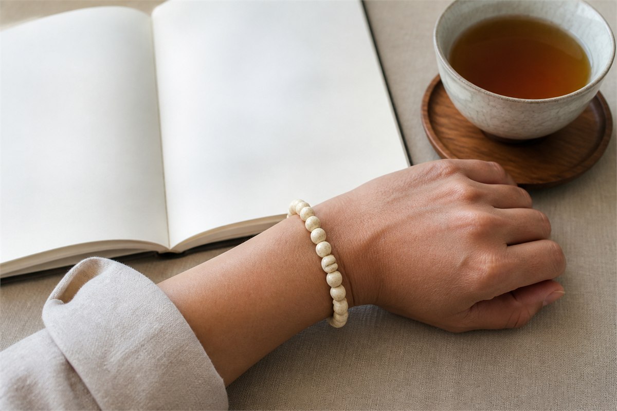 Adult wrist wearing a small bone bead bracelet beside a blank notebook and tea cup