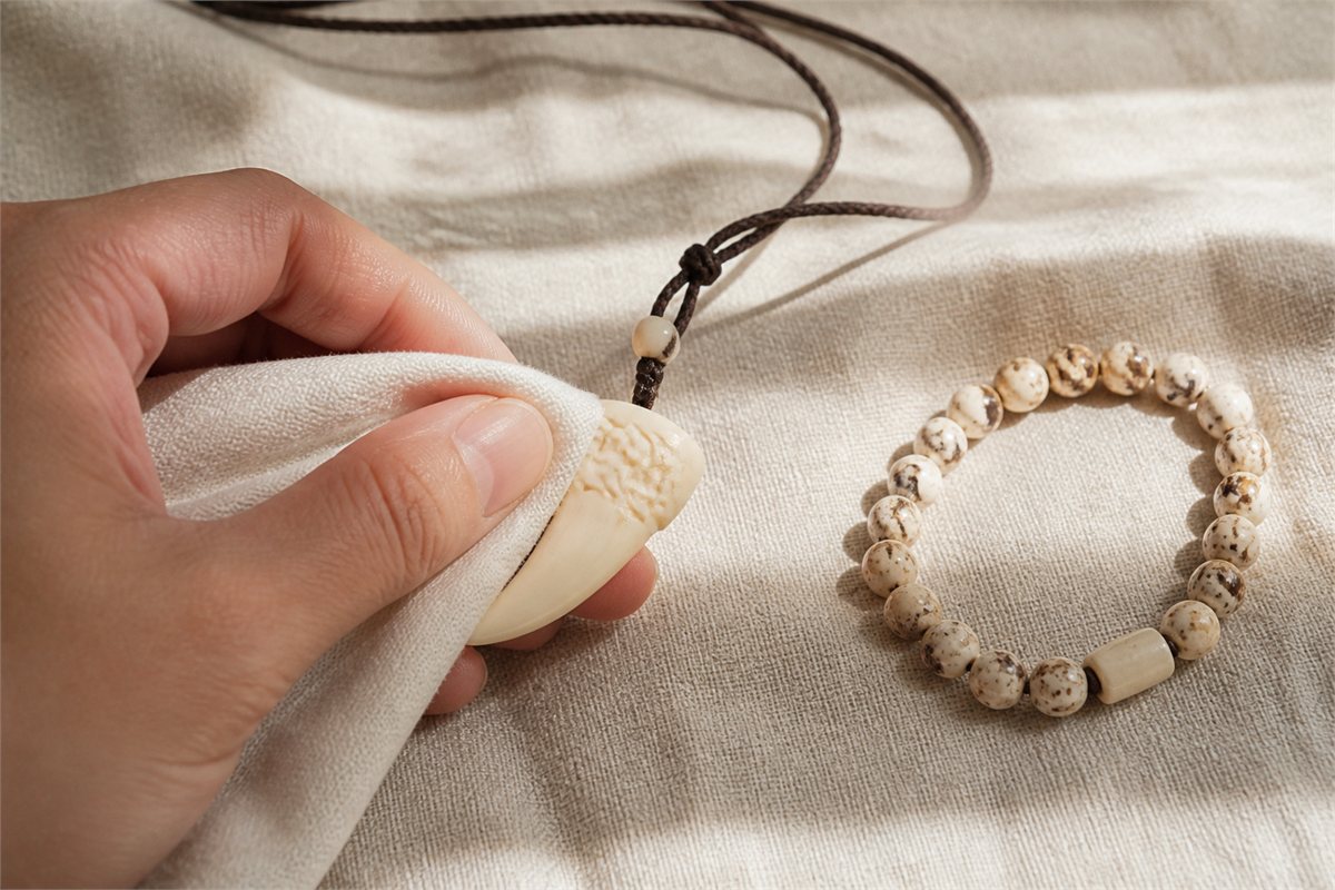 Hand gently wiping a finished pale bone pendant with a clean soft dry cloth