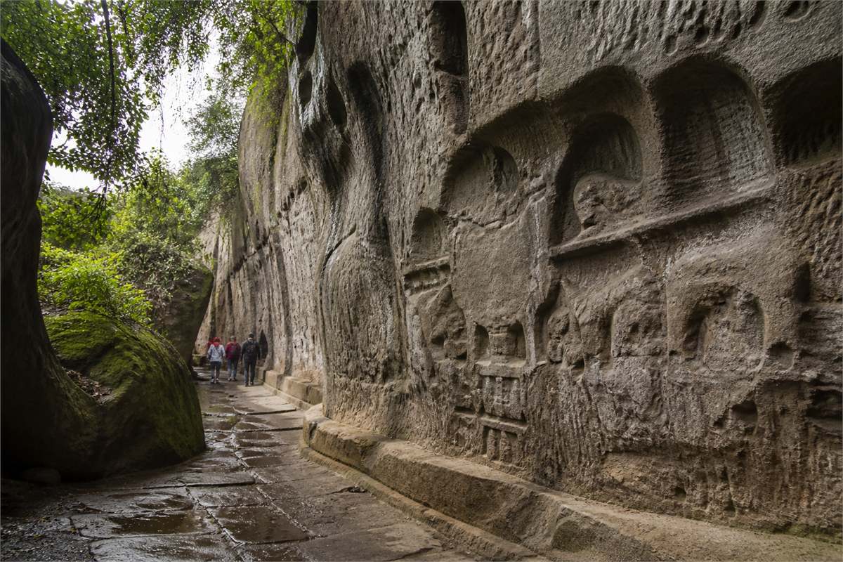 Weathered sandstone cliff passage with shallow reliefs and distant visitors