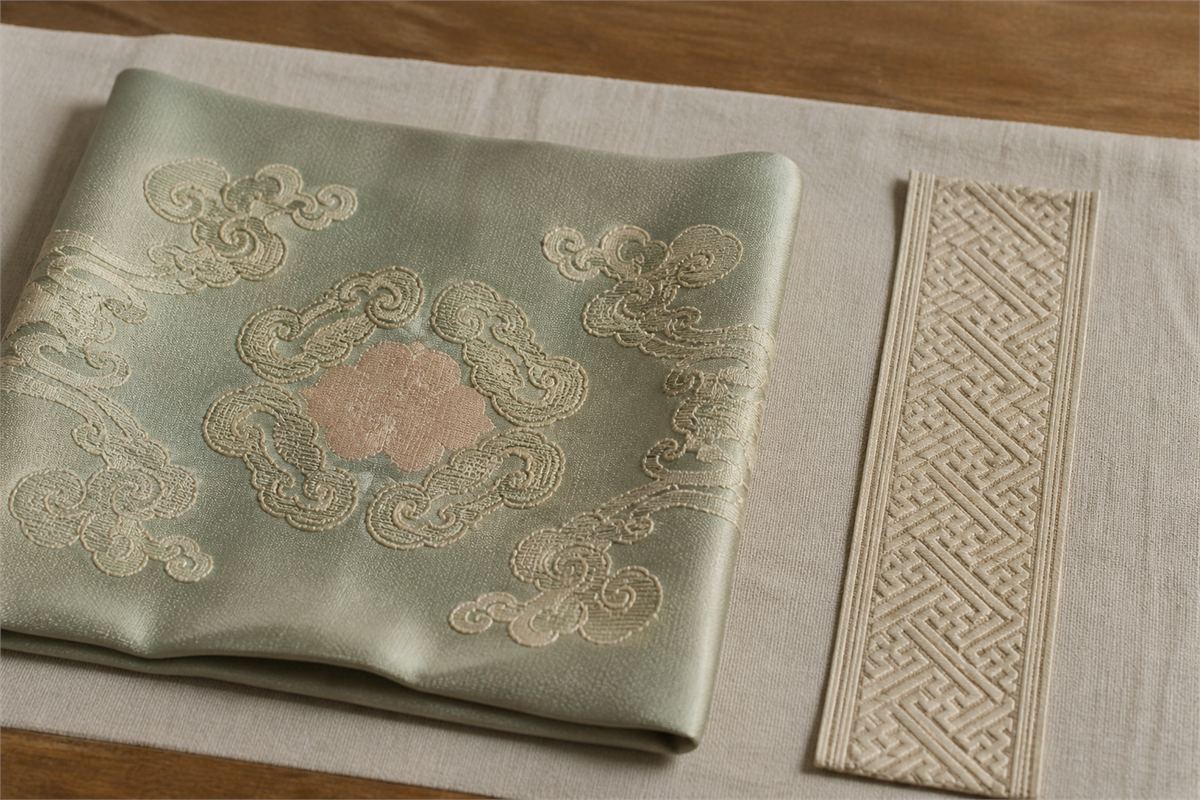 Muted green silk with cloud scroll embroidery beside a separate cream continuous geometric border