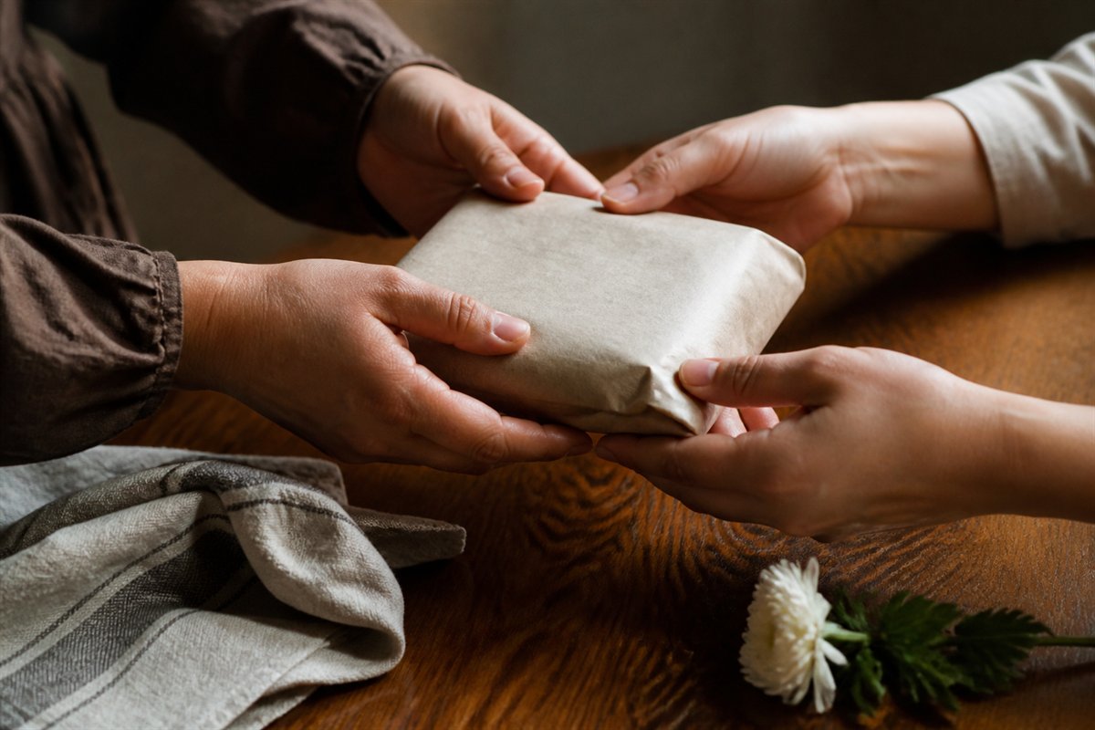 Four hands carefully passing a plain food parcel across a wooden table