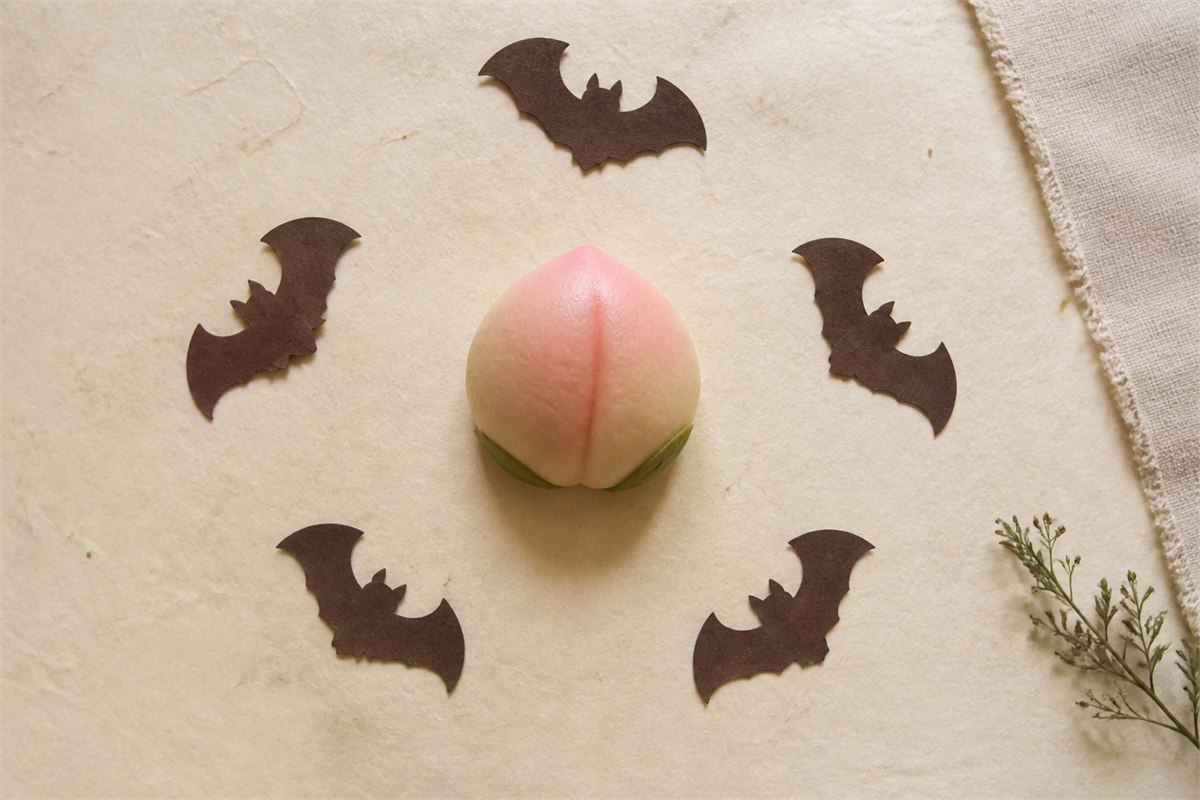 Five dark paper bat silhouettes surrounding a peach-shaped birthday bun on handmade paper