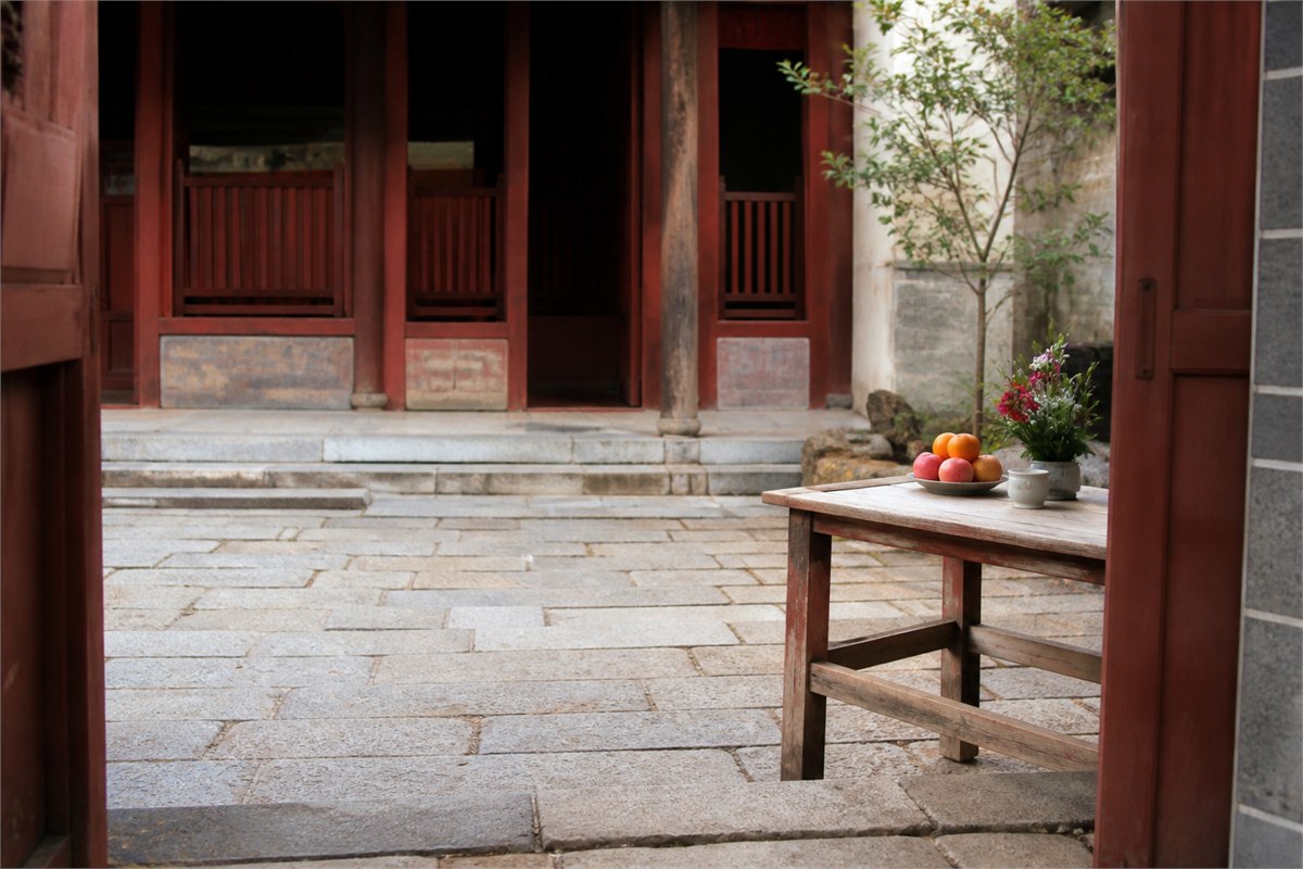 Quiet red-wood courtyard with fruit and flowers on a simple offering table